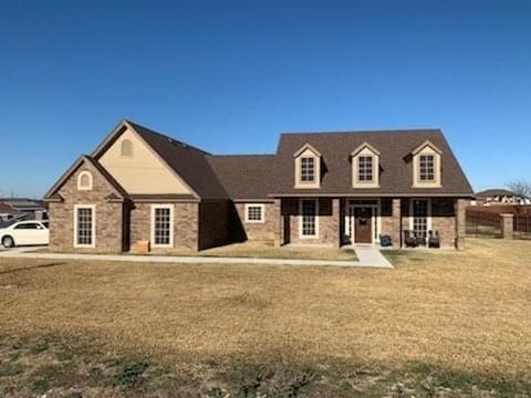 A single-story, tan brick house with three roof dormers and a brown shingled roof under a clear blue sky.