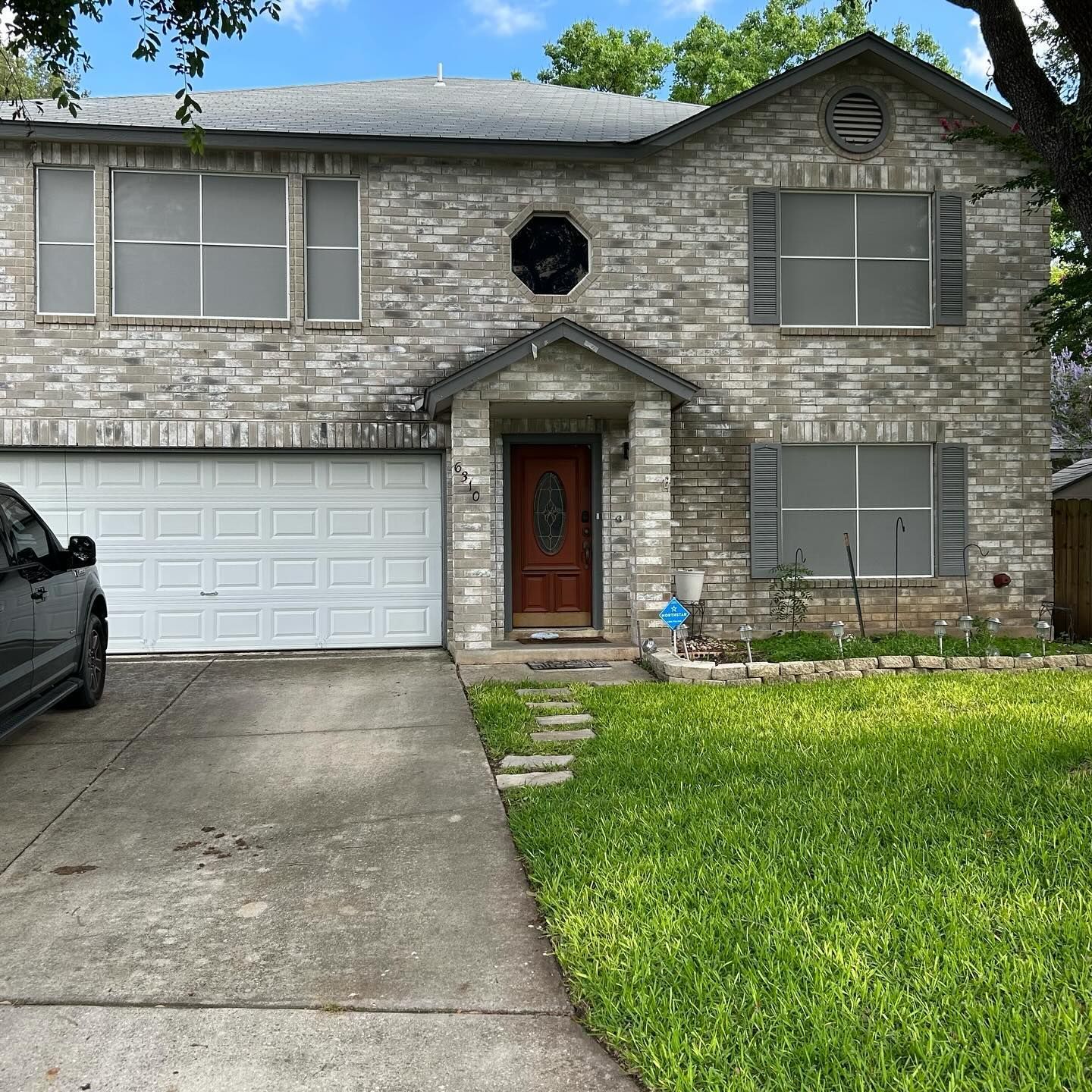 A two-story house with light-colored stone siding, a brown front door, an octagonal window, and a white garage door.