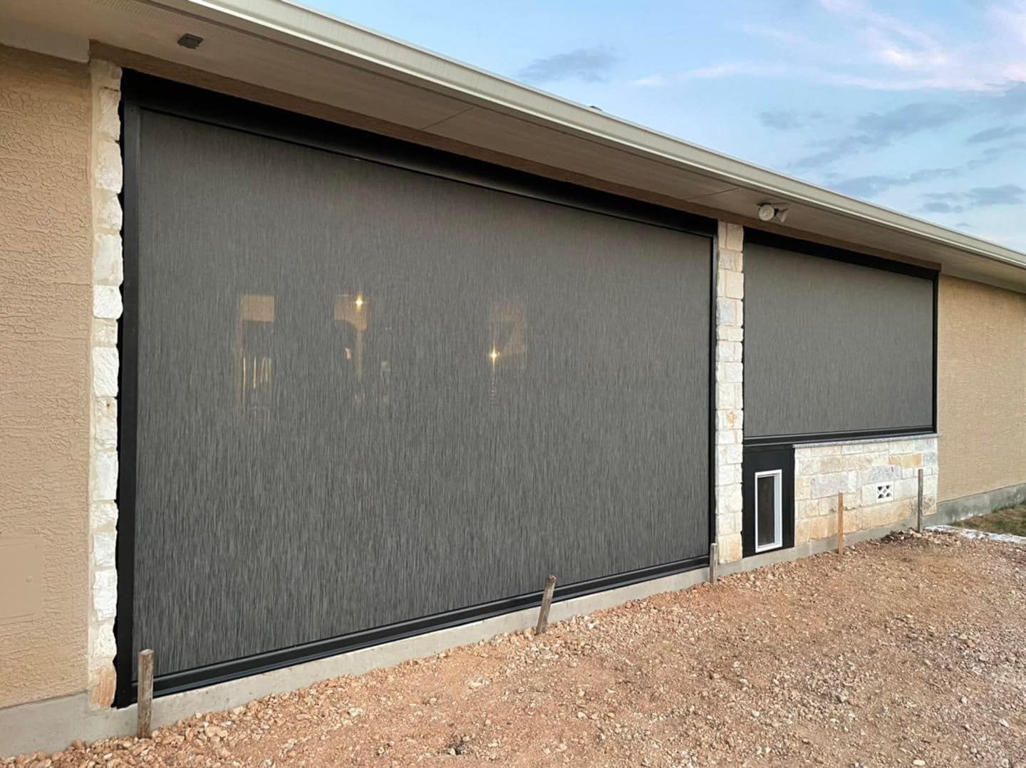 Dark, retractable solar screens are installed on the stone and stucco exterior of a residential patio.