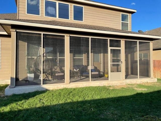 A tan, two-story house featuring a large, ground-level screened-in porch with a door, facing a grassy backyard.