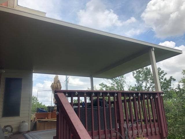 A covered patio with a wooden railing and string lights, overlooking an outdoor space under a partly cloudy sky.