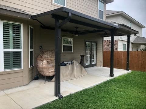 A tan house features a dark covered patio with a ceiling fan, a hanging chair, and a concrete floor.