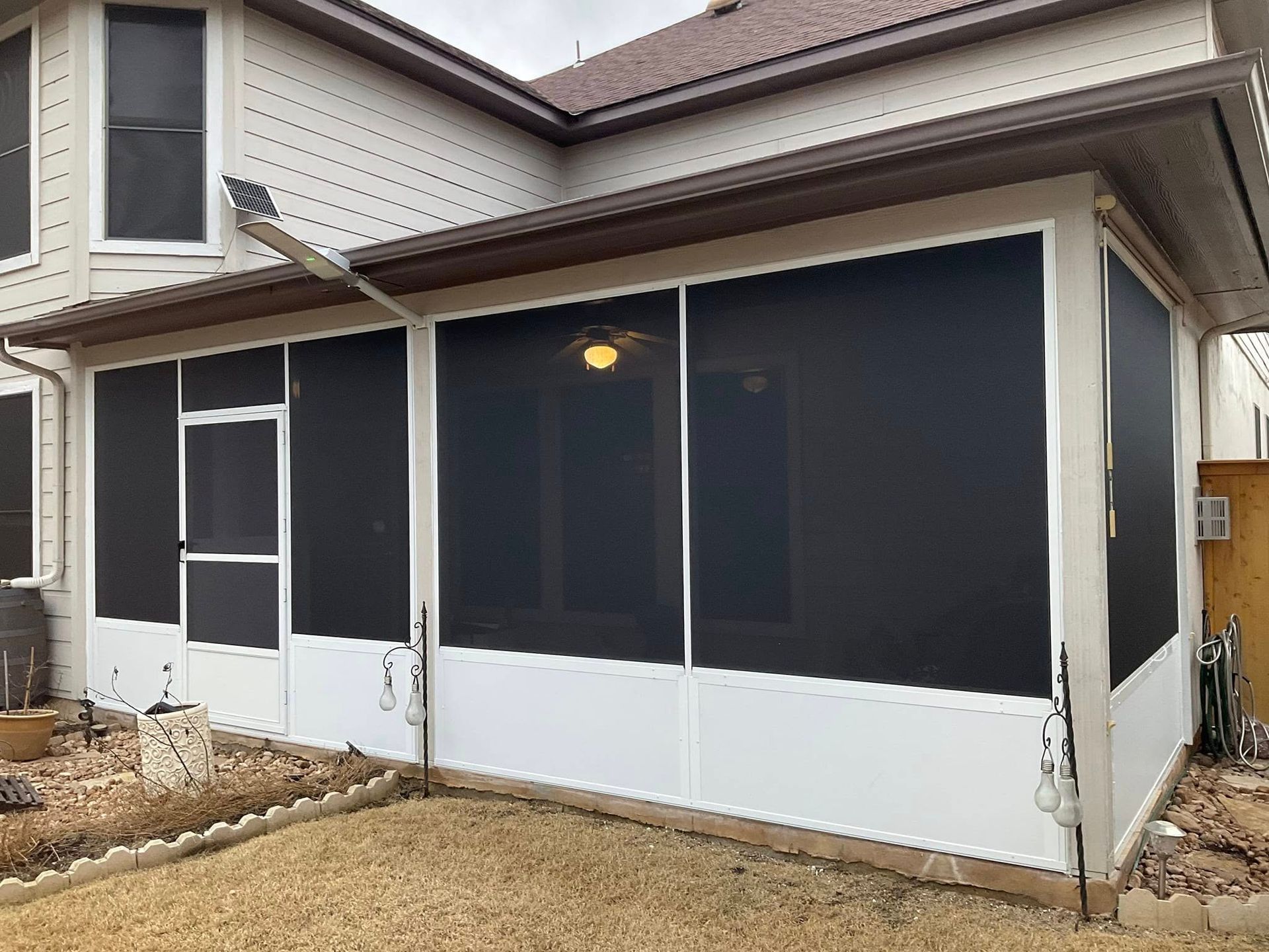A sunroom addition with white frames and black screens attached to the rear exterior of a house.