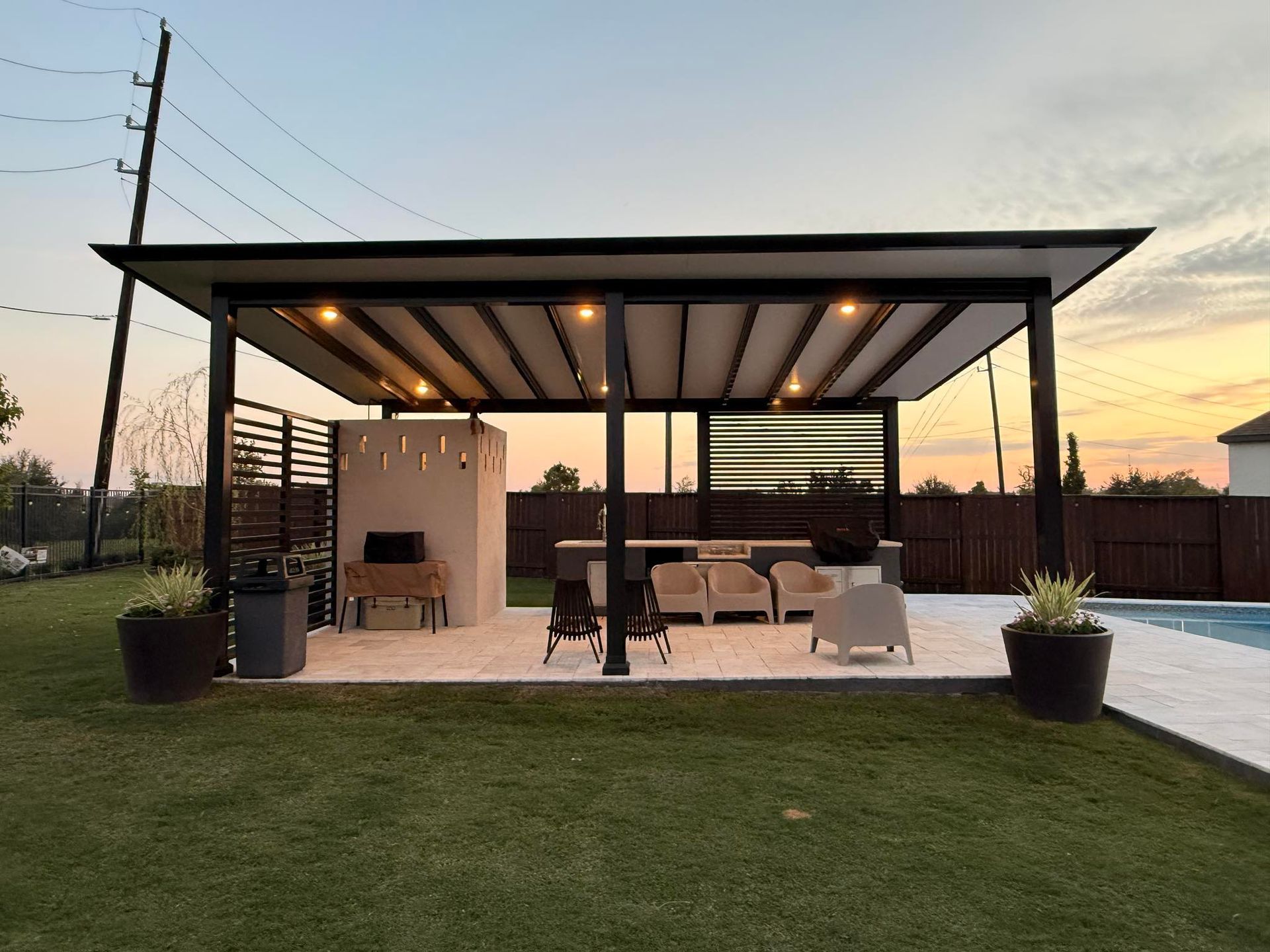 Modern outdoor patio featuring a black-framed pergola with recessed lighting over lounge furniture near a swimming pool.