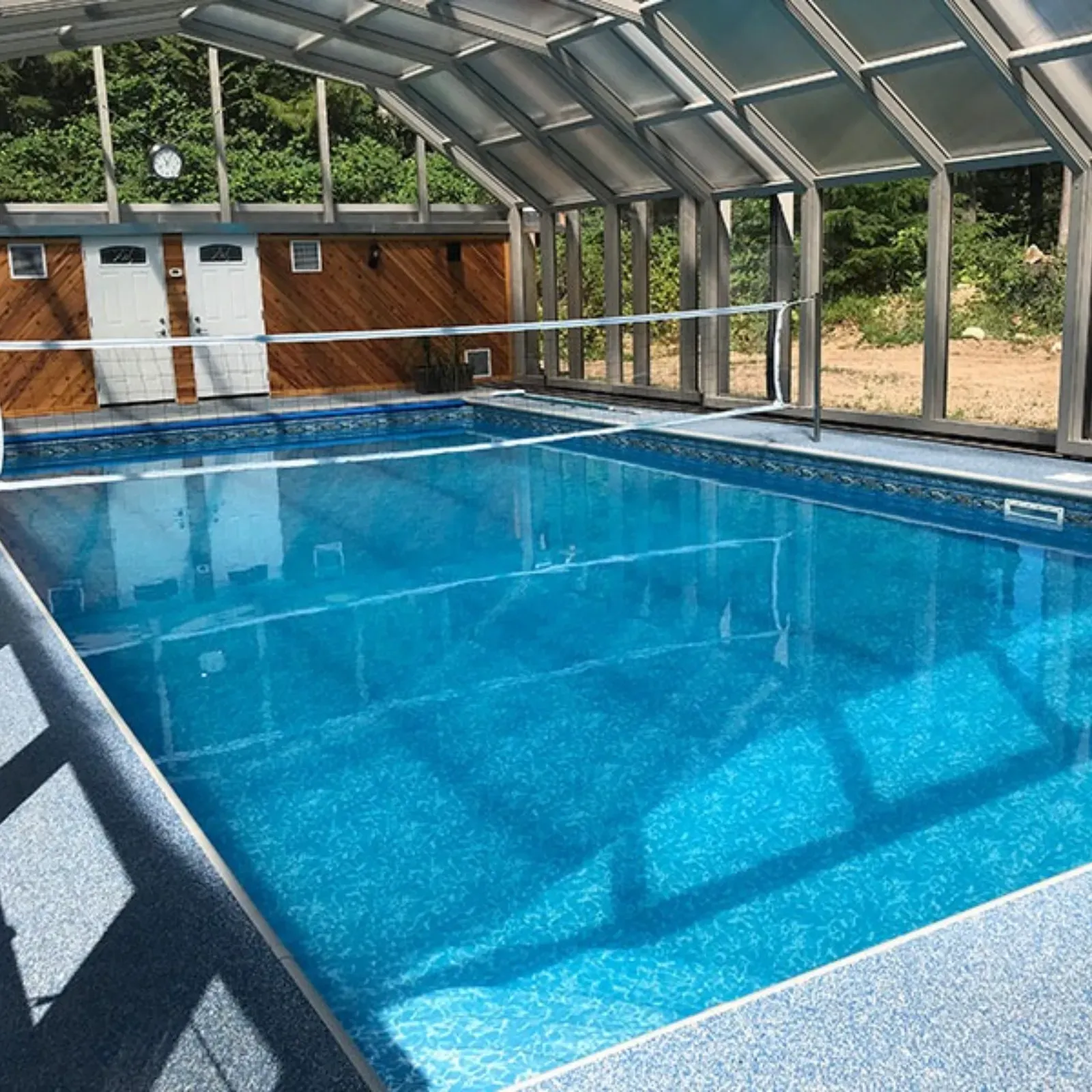 A rectangular swimming pool with three water fountains features a stone deck, enclosed by a black screened cage.