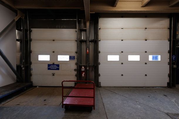 Deux portes de garage industrielles blanches fermées, un chariot rouge et des poutres de soutien métalliques.
