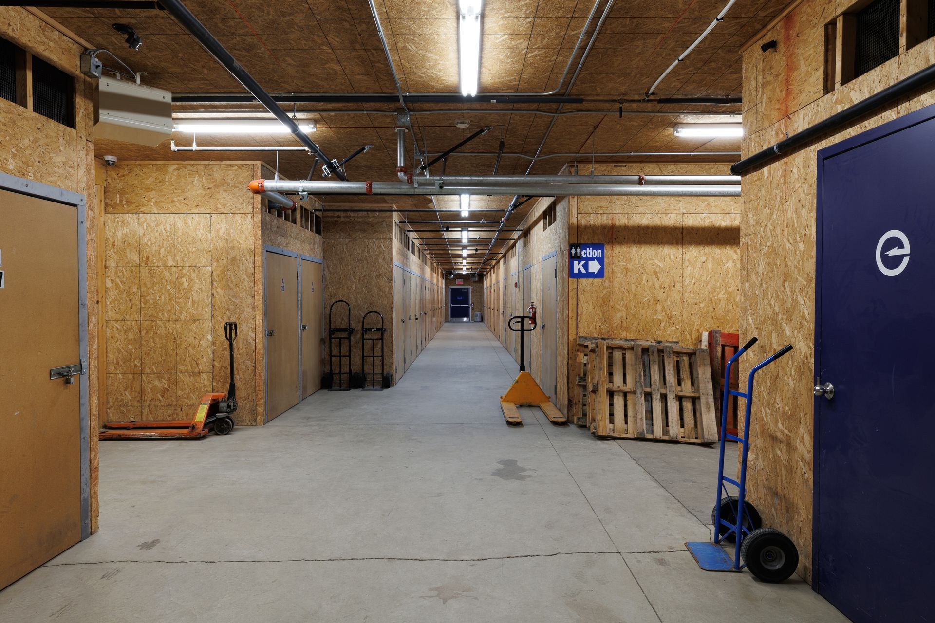 Long couloir d'entrepôt vide, avec murs et plafond en bois et portes des deux côtés.