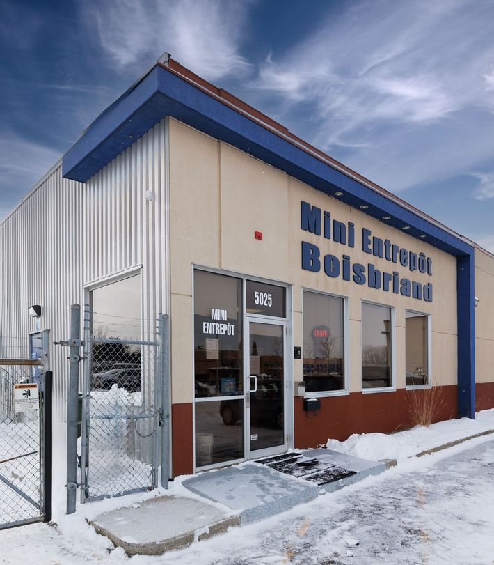 Vue extérieure de l'entrepôt « Mini Entrepôt Bolsbriand » par temps de neige ; bâtiment bleu, beige et rouge brique.