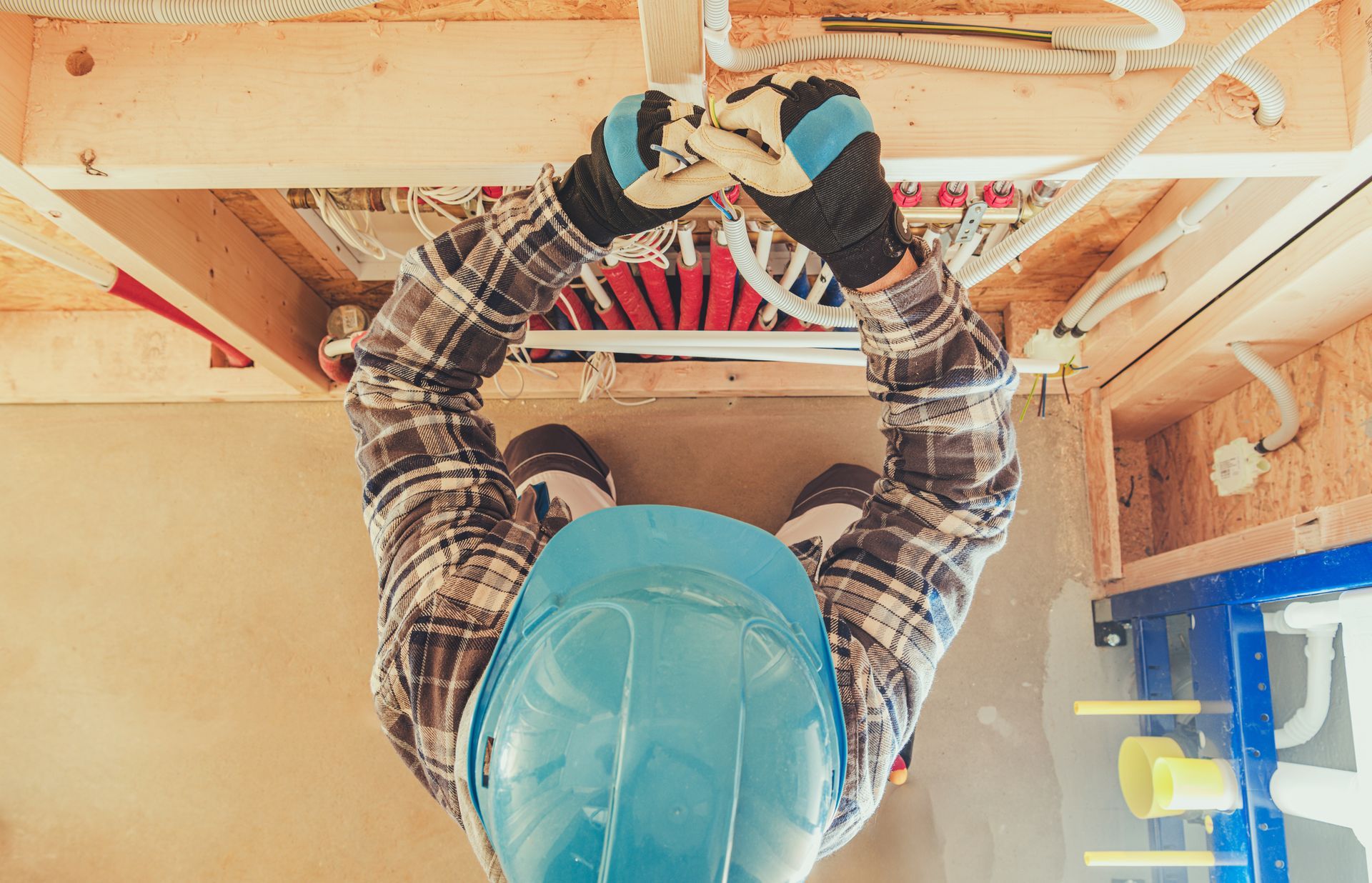 Worker in a hard hat organizing electrical wires inside a wall opening.