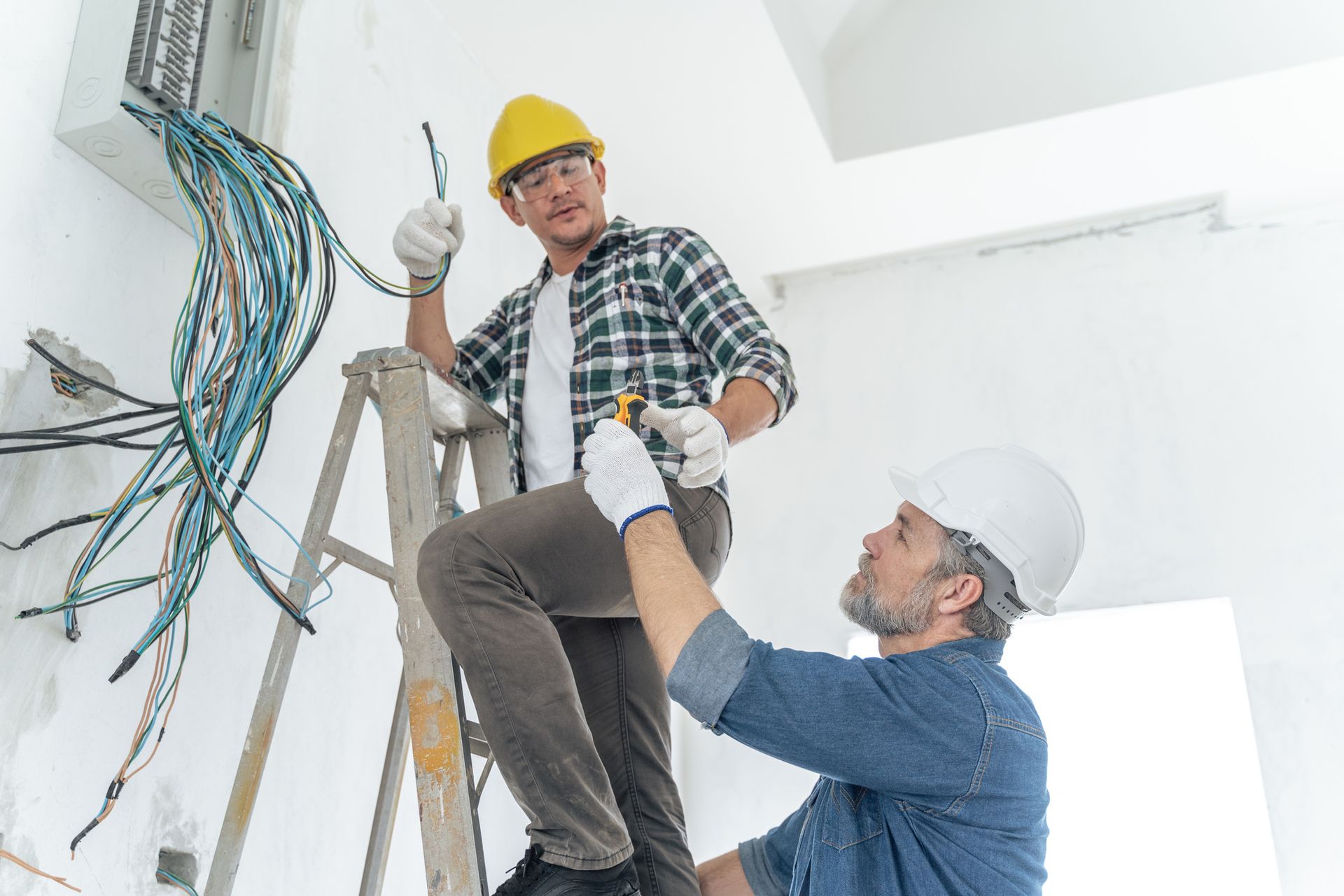 Electricians working on high-voltage cables near an open electrical panel.