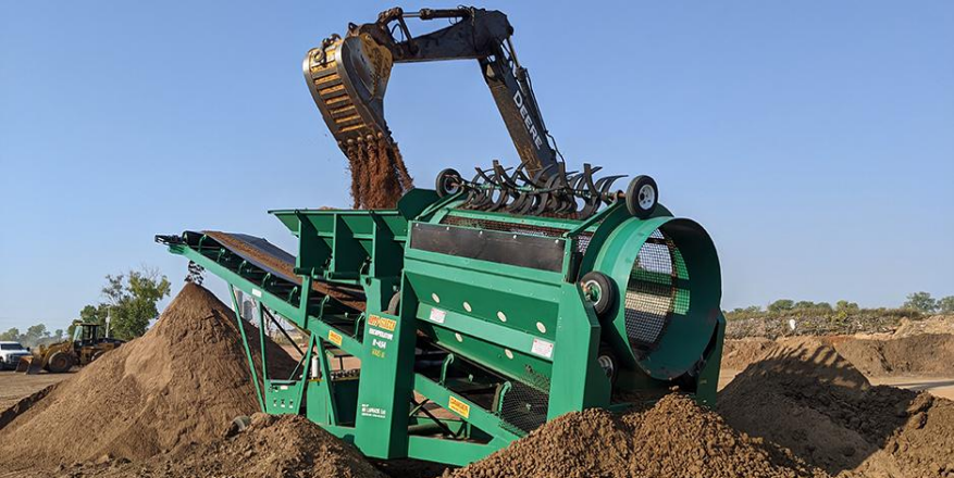 A green machine is sitting on top of a pile of dirt.