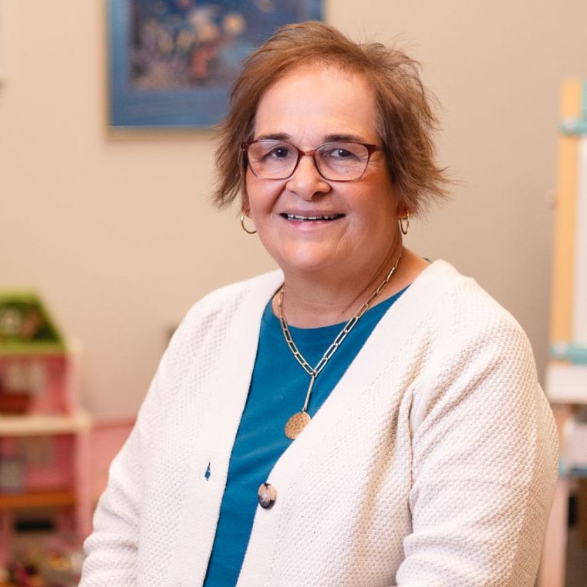 A woman wearing glasses and a blue shirt is smiling for the camera