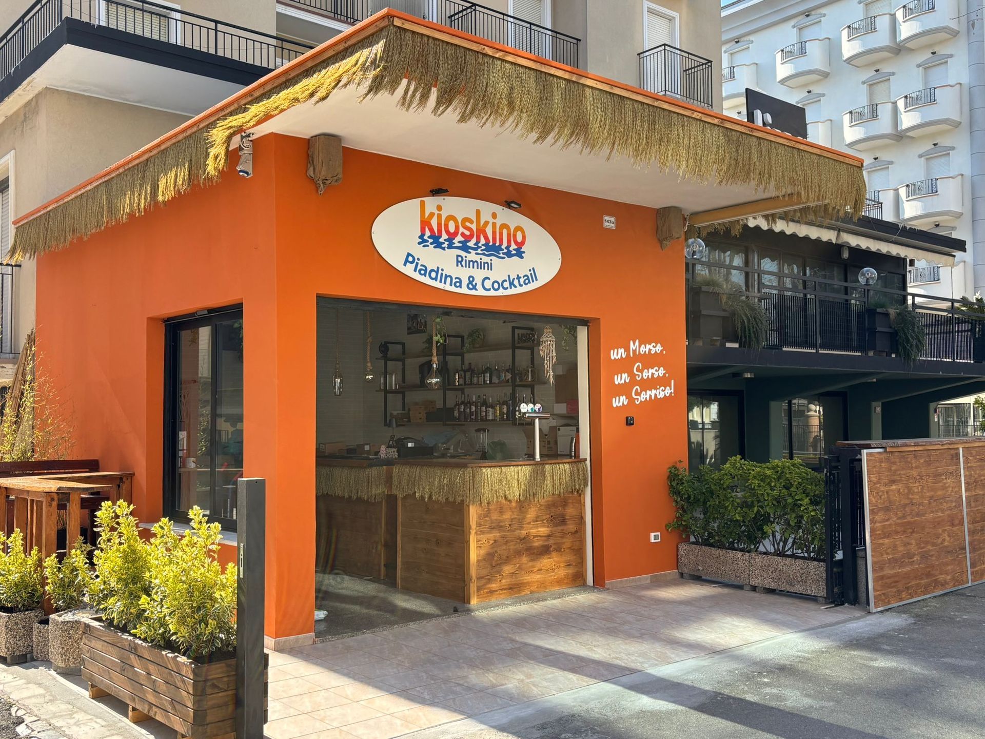 Un bar all'aperto con pareti arancioni, tetto di paglia e un'insegna con la scritta