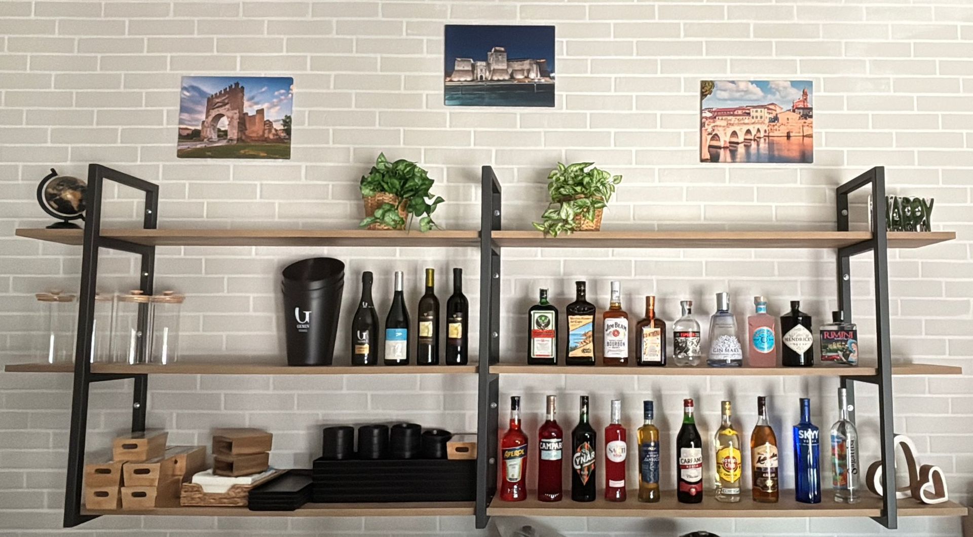 Scaffale con tre cornici portafoto sopra, pieno di bottiglie di vino e liquori di vario tipo, bicchieri e oggetti decorativi.