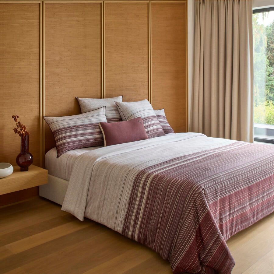 Une chambre moderne avec un lit paré de draps rayés bordeaux et beige, des lambris au mur et des rideaux drapés.