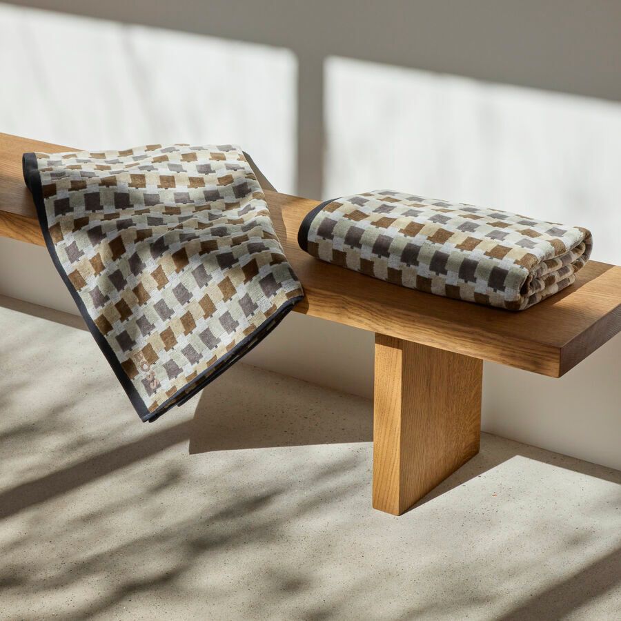 Deux couvertures pliées à motifs à carreaux beiges, marrons et blancs reposent sur un banc en bois.
