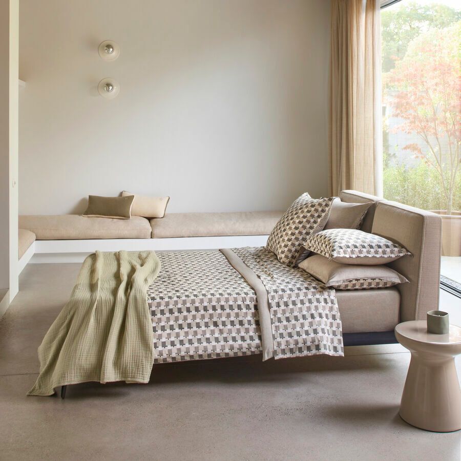 Une chambre moderne avec un lit doté de draps à motifs, un jeté de lit vert et une banquette intégrée sous une fenêtre.