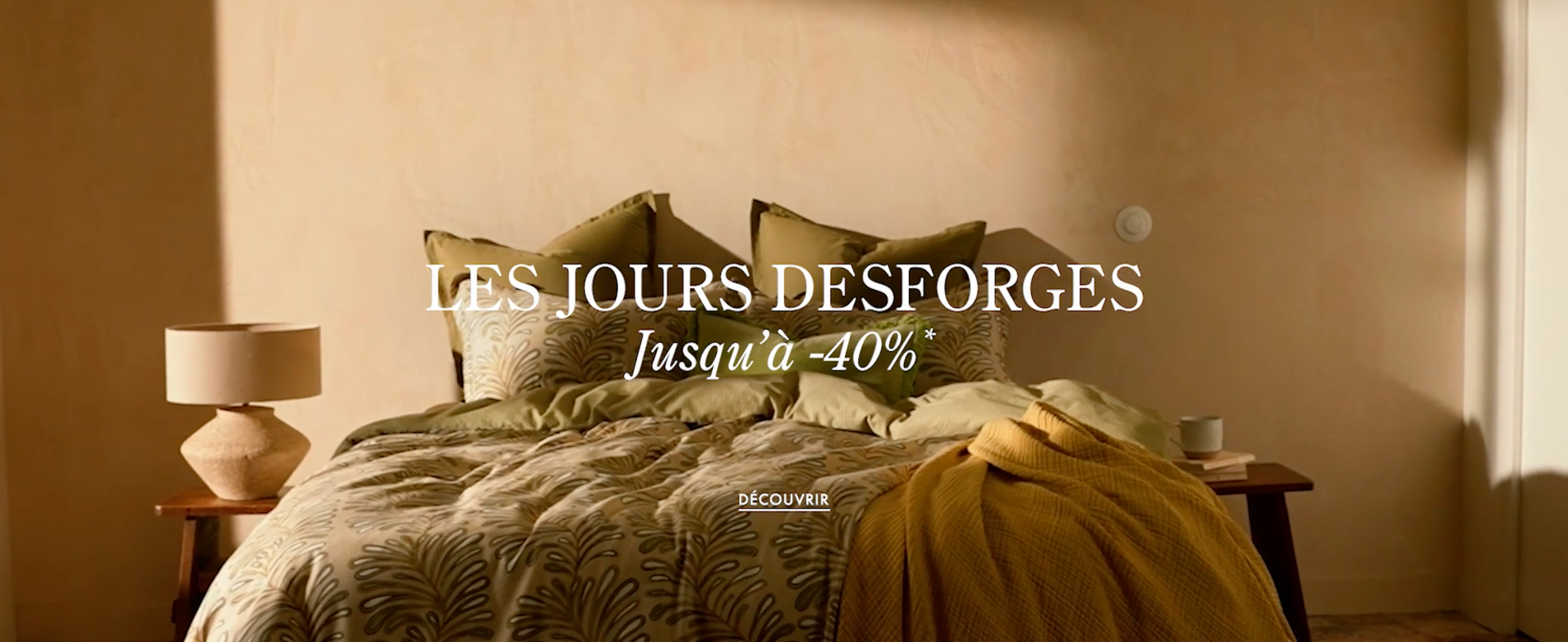 Une chambre confortable avec une couette verte à motifs, des oreillers et un plaid jaune, annonçant une réduction allant jusqu'à 40 %.