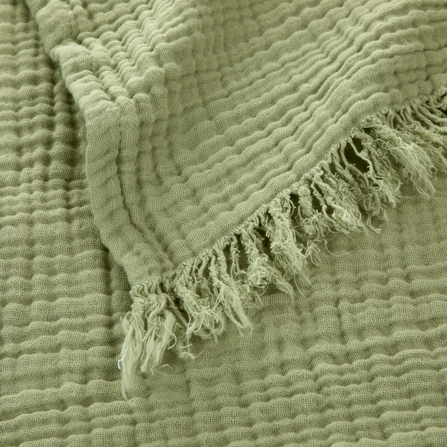 Gros plan sur un tissu de mousseline de coton vert sauge, froissé, avec un bord effiloché et frangé.