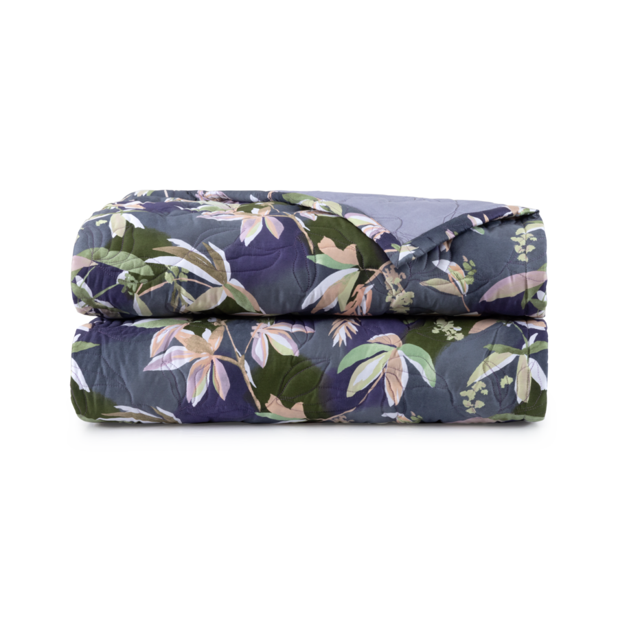Couverture pliée à motif floral dans les tons de bleu, de vert et de beige.