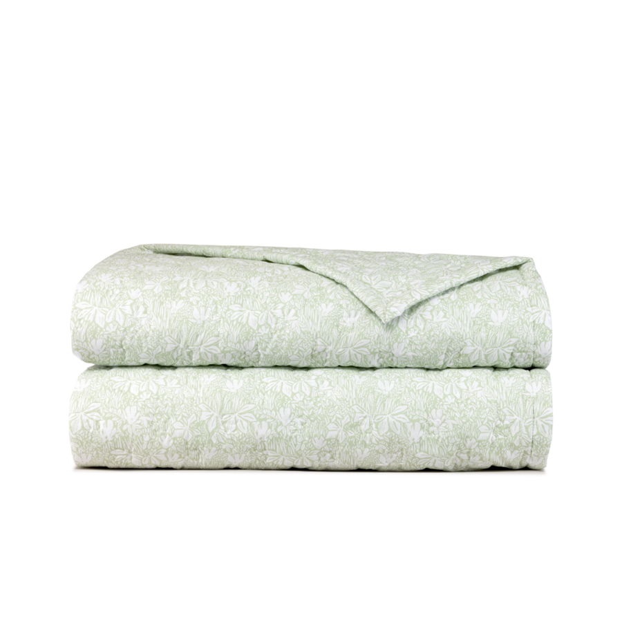 Une couverture pliée, vert clair, ornée d'un motif botanique ou floral discret et répétitif sur fond blanc uni.