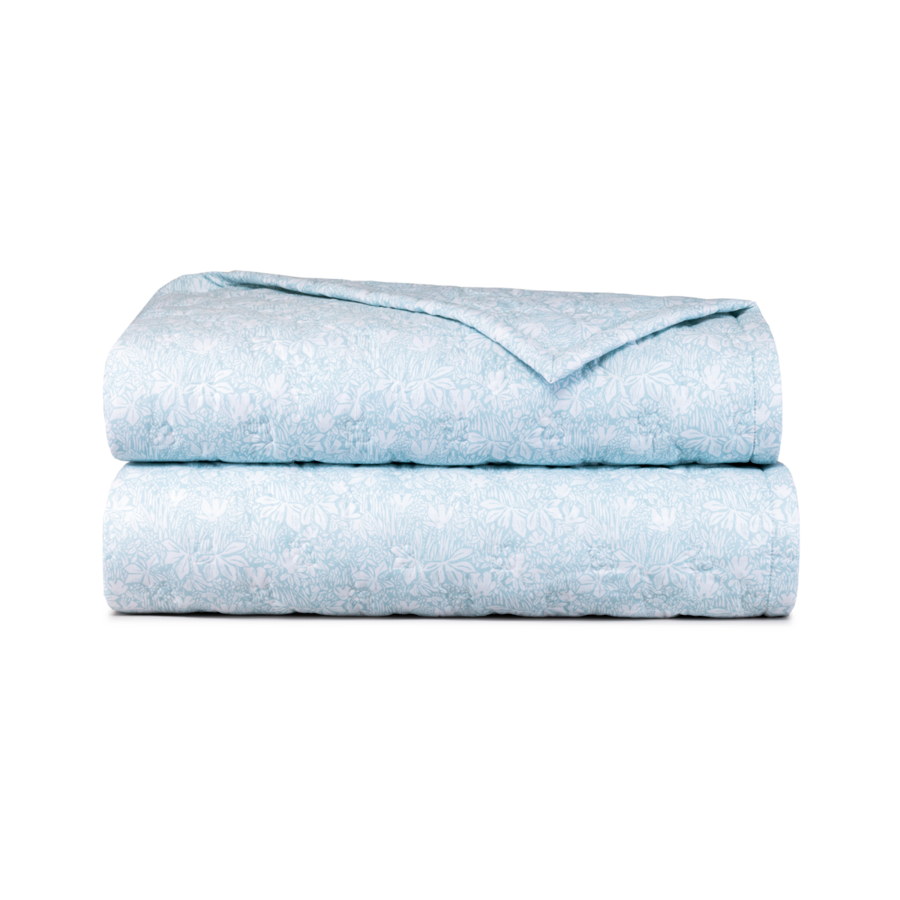 Une couverture matelassée bleu clair, soigneusement pliée en une pile rectangulaire sur un fond blanc uni.