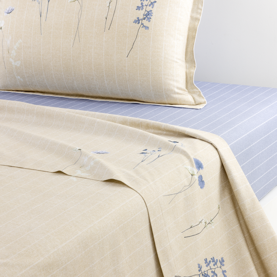 Un drap-housse et une taie d'oreiller beiges à motifs floraux bleus, contrastant avec un drap-housse bleu clair à fines rayures.