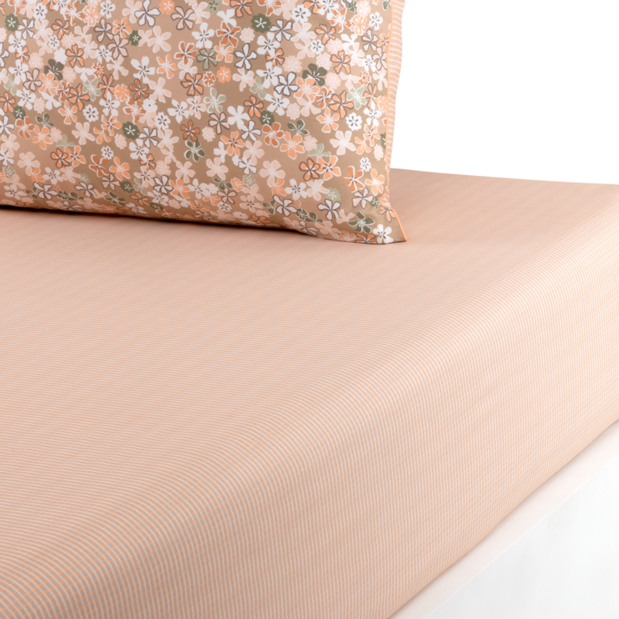 Un coussin à motifs floraux posé sur un drap-housse côtelé rose clair, sur fond blanc.