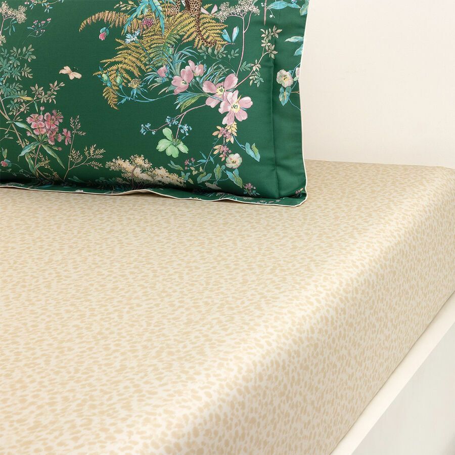 Coussin à fleurs vertes sur un drap beige à pois.