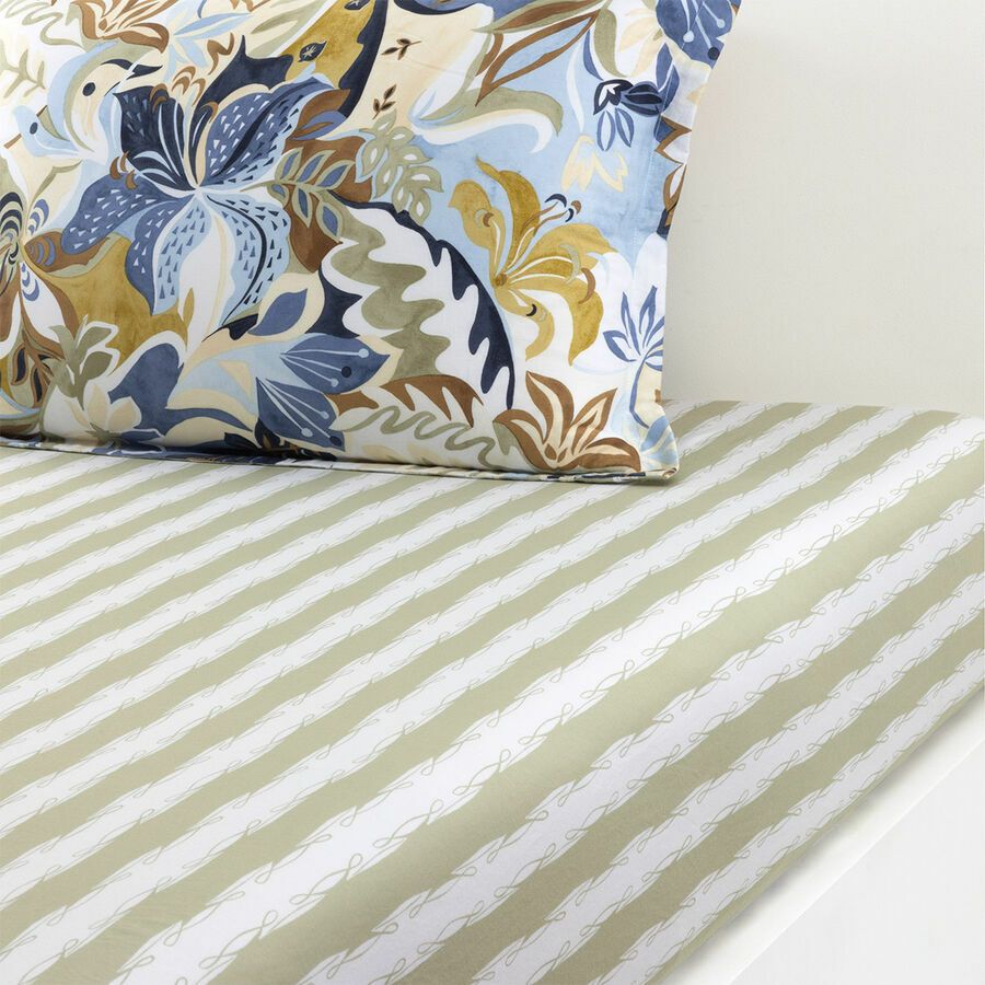 Pillow with blue floral pattern on bed with white and khaki striped sheet.