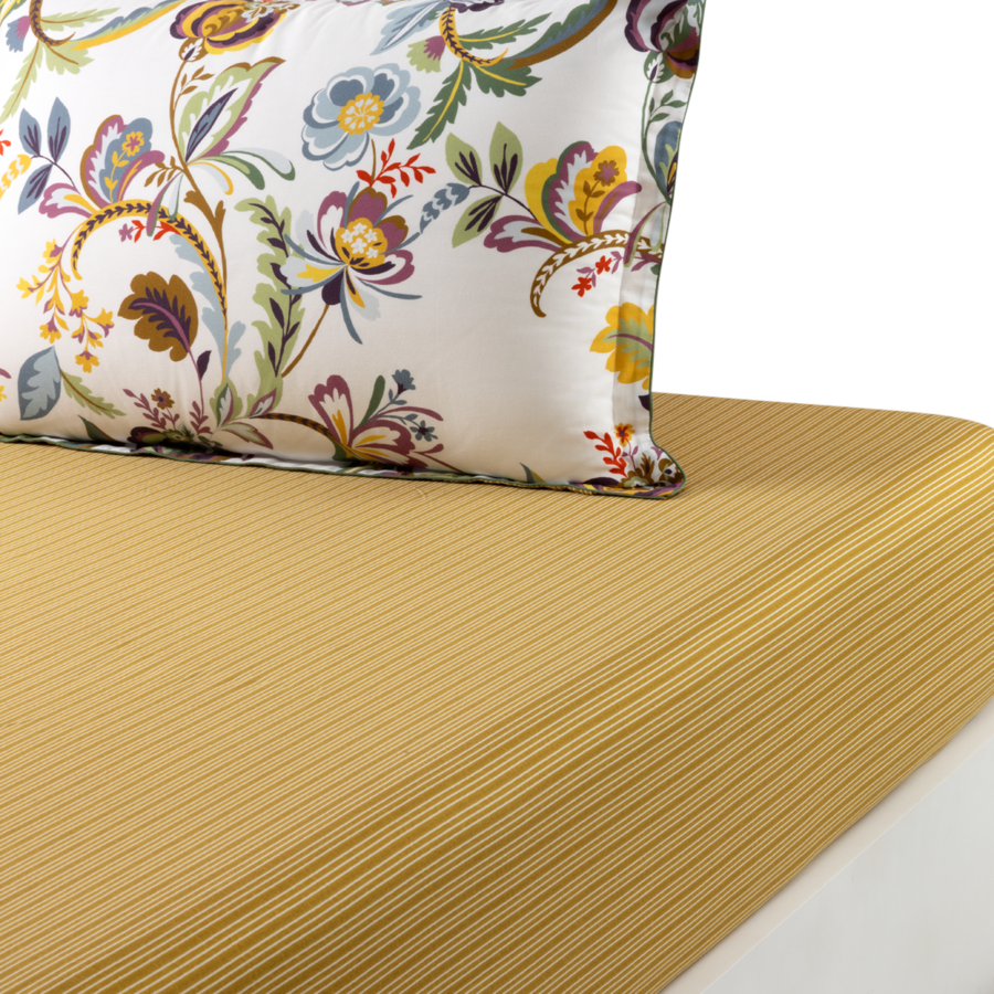 Un oreiller blanc à motifs floraux colorés repose sur un lit recouvert d'un tissu texturé jaune doré.