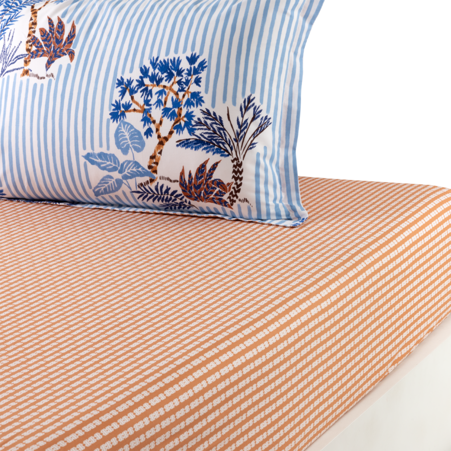 Un coussin à rayures bleues et blanches orné d'un motif botanique repose sur un drap-housse à rayures orange et blanches.