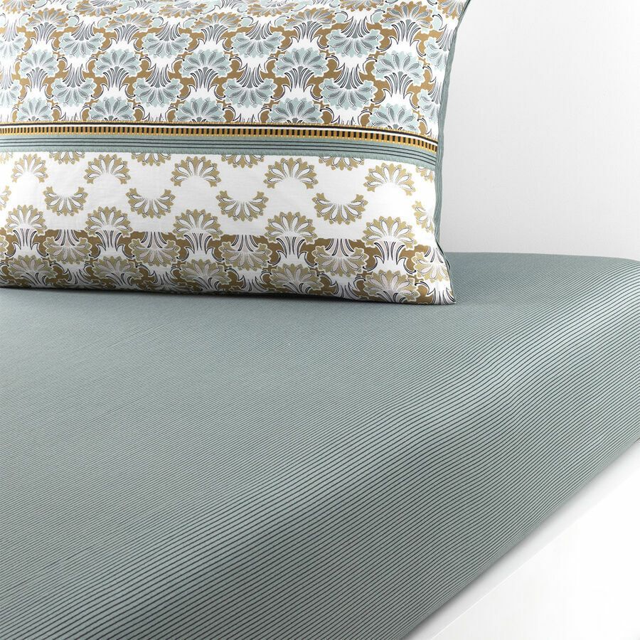 Un coussin à motifs repose sur une surface texturée bleu pâle.