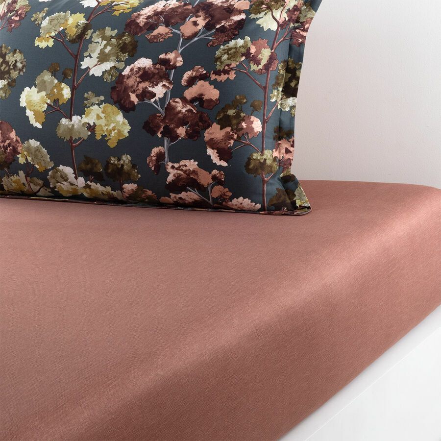 Rose-colored fitted sheet with a floral patterned pillow on a white surface.