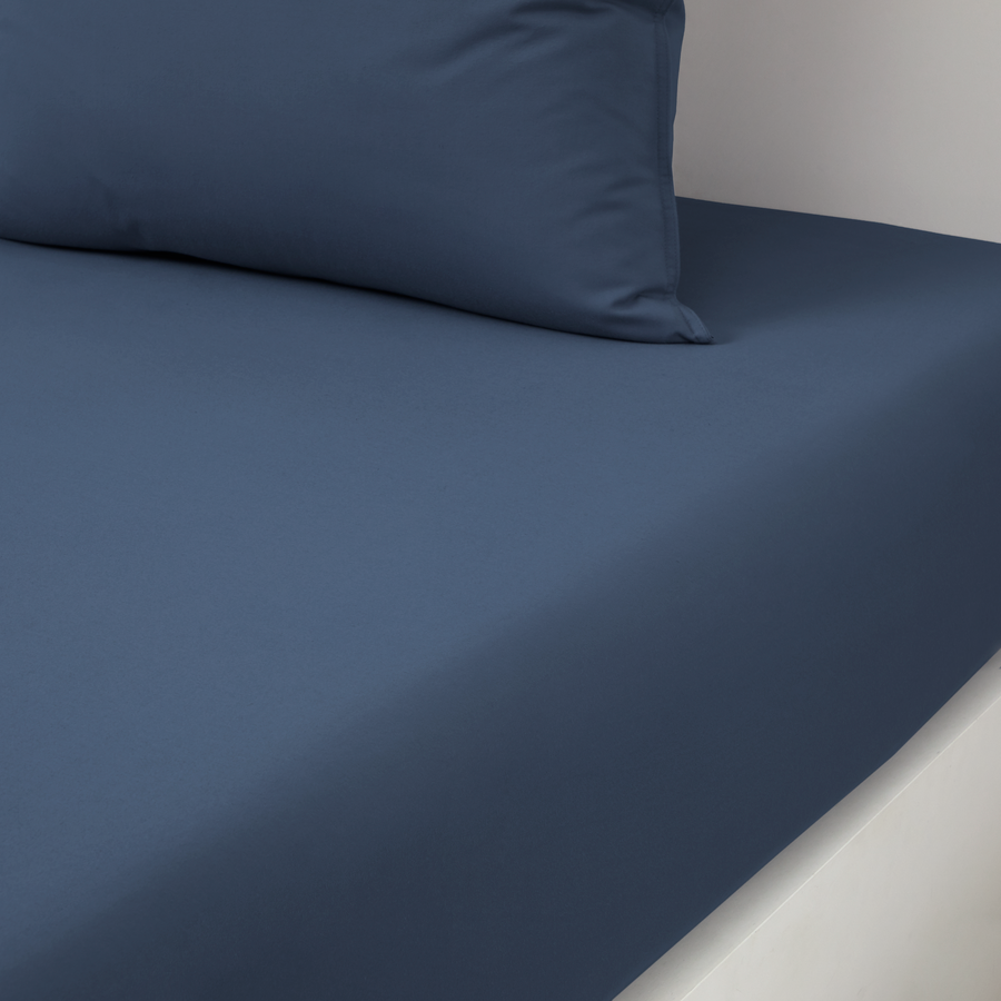 Un drap-housse bleu recouvre un matelas, laissant apparaître un oreiller bleu assorti sur le dessus.