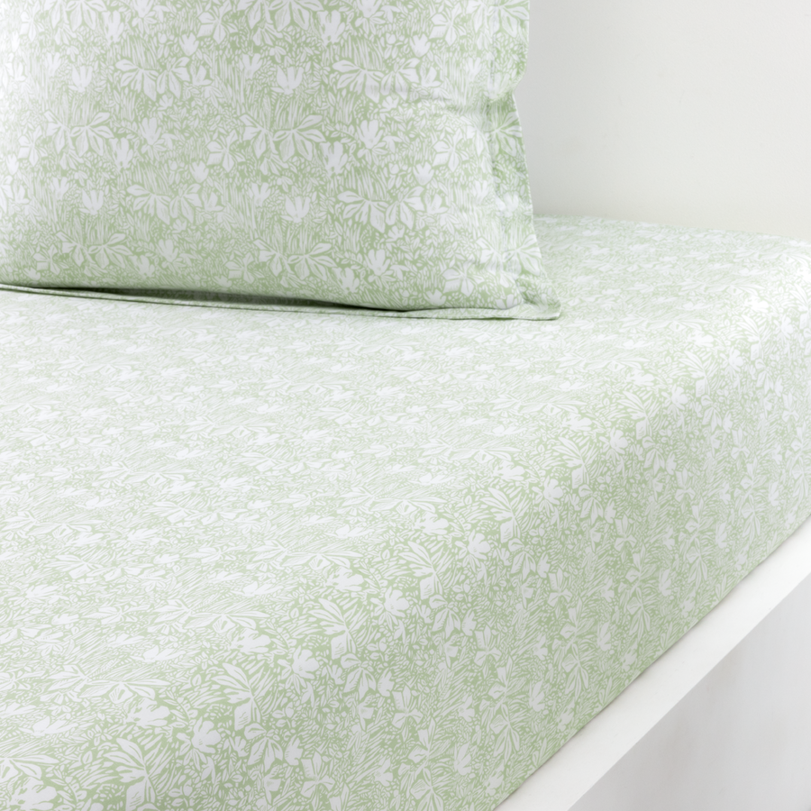 Un drap-housse à motifs floraux vert sauge et blancs et une taie d'oreiller assortie sur un lit.