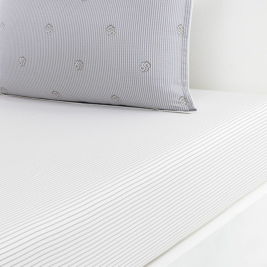 Gros plan sur un drap blanc à fines rayures grises, à côté d'un oreiller assorti, devant un mur blanc.