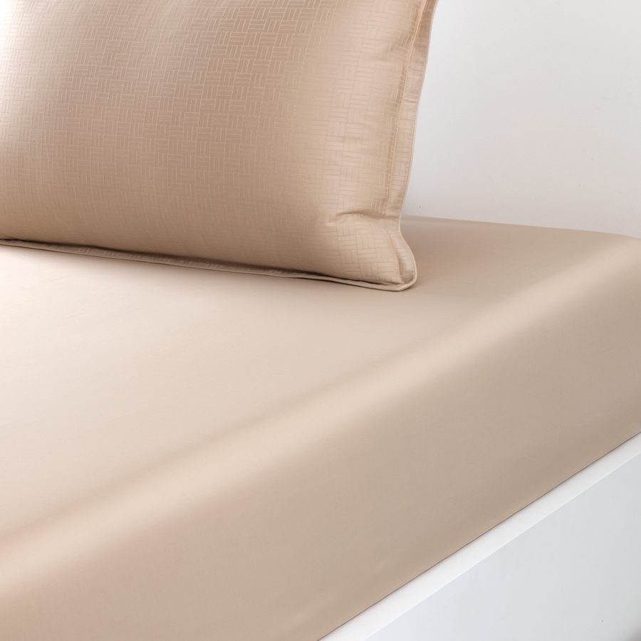 Un oreiller couleur beige repose sur un drap-housse lisse assorti, recouvrant le lit.