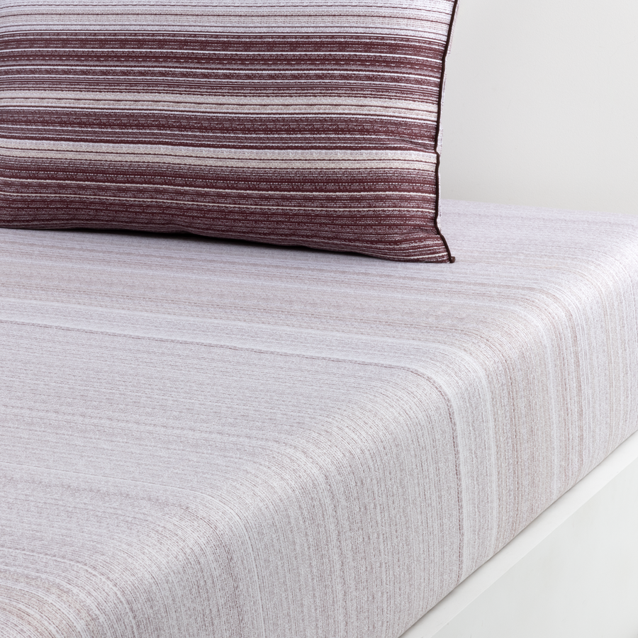 Un drap-housse gris clair texturé recouvre un matelas, contre lequel repose un oreiller foncé à rayures horizontales.