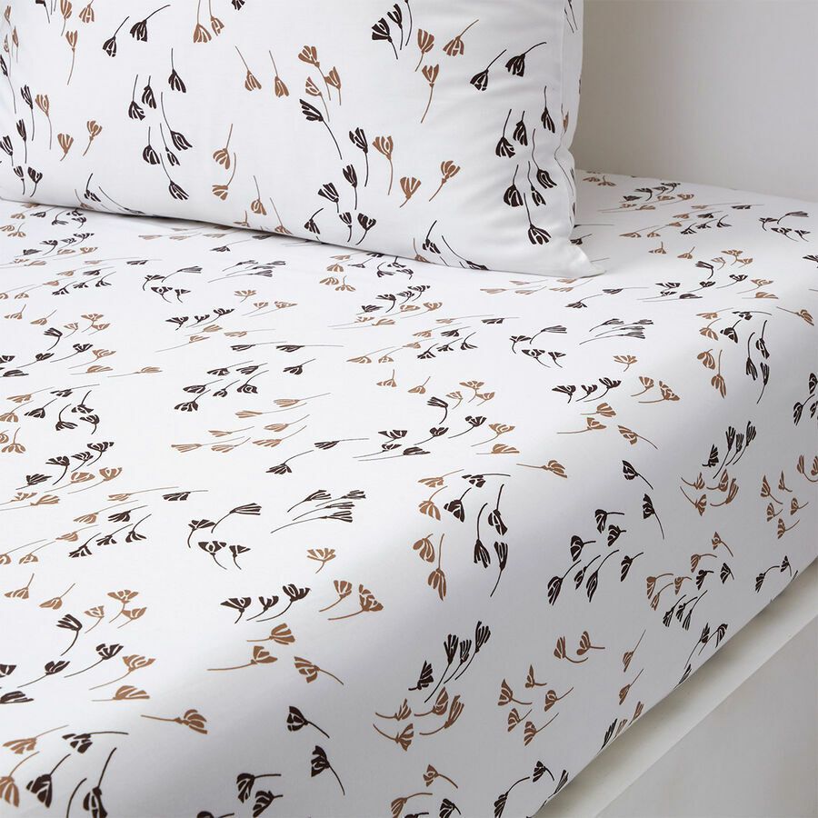 Draps de lit et taie d'oreiller blancs ornés d'un délicat motif répétitif de petites fleurs brun foncé et noires dessinées à la main.