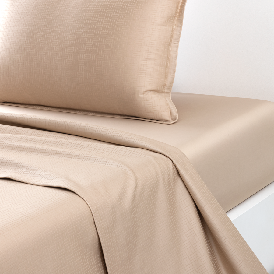 Des draps beiges et un oreiller assorti sur une surface blanche.