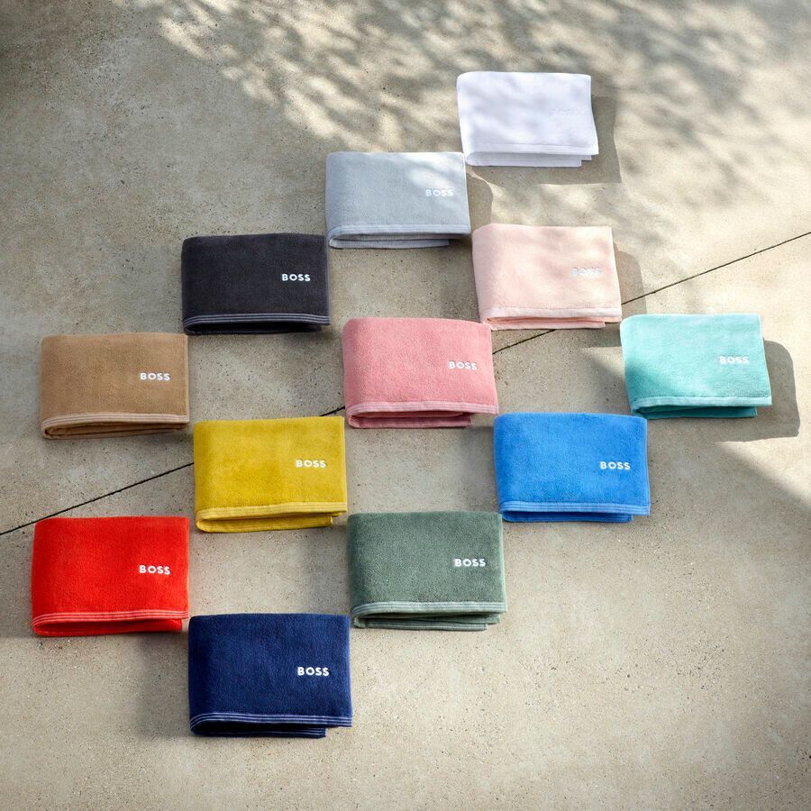 Une collection de serviettes rectangulaires pliées, de couleurs unies variées, chacune portant la marque « BOSS » imprimée sur le bord.