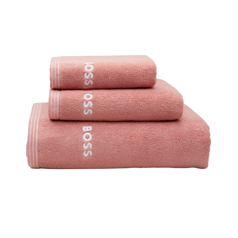 Une pile de trois serviettes rose poudré, chacune portant le logo « BOSS » en blanc et un ourlet rayé, isolée sur un fond blanc.
