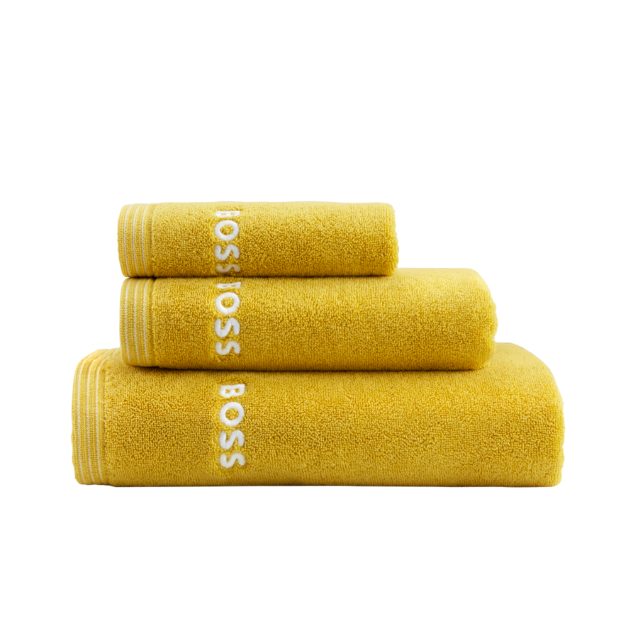 Trois serviettes de bain jaunes empilées, chacune brodée du nom de la marque « BOSS » en lettres blanches.