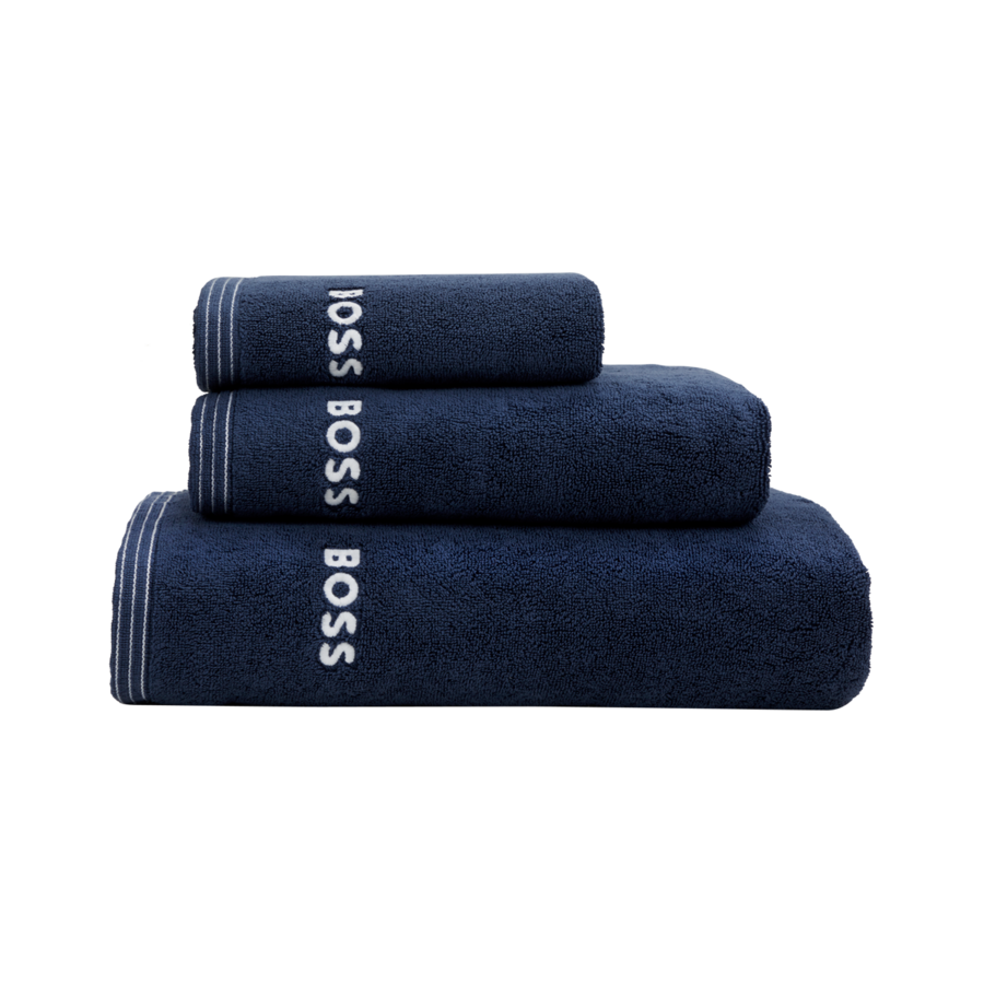 Une pile de trois serviettes bleu marine, chacune ornée du logo Hugo Boss blanc et d'une bordure rayée.