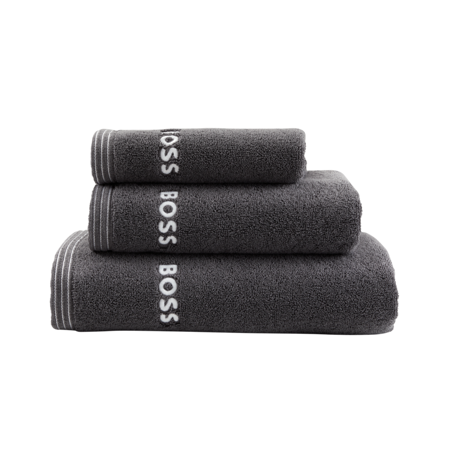 Une pile de trois serviettes de toilette gris foncé de marque BOSS, pliées et classées par taille, sur fond blanc.