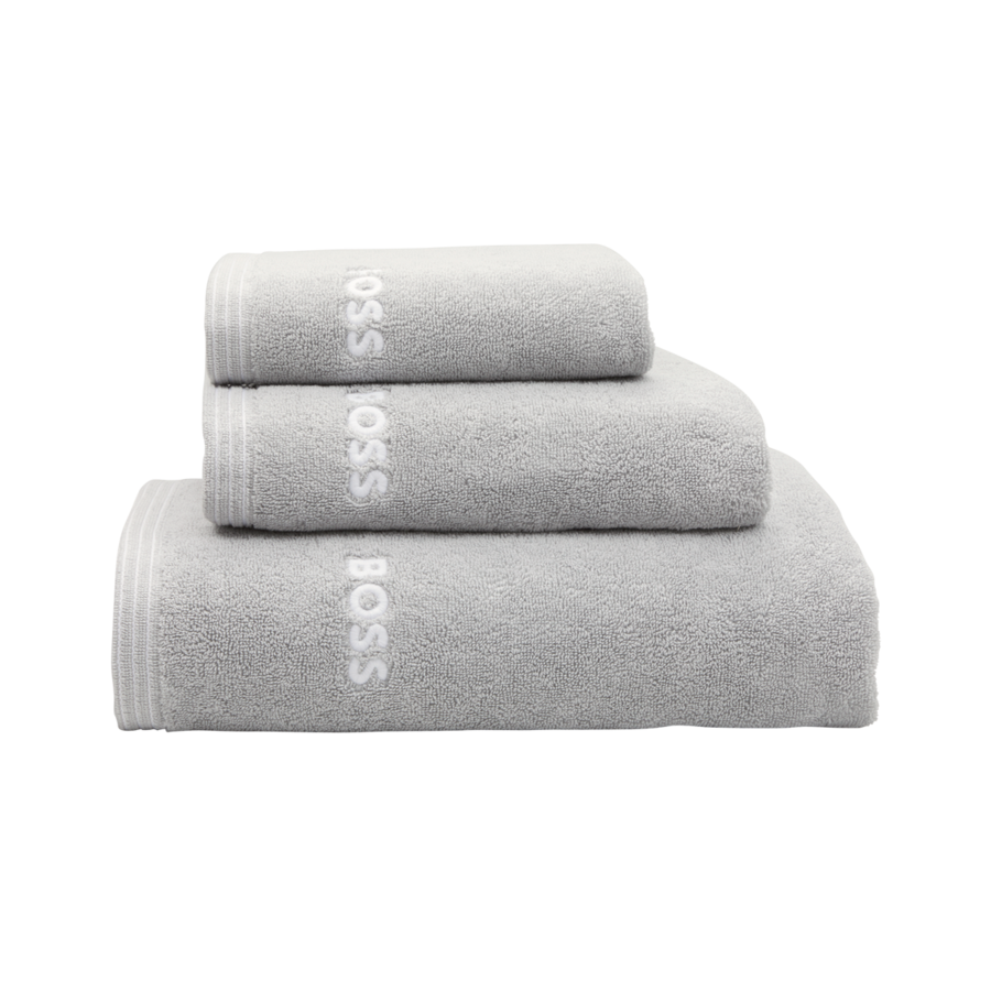 Trois serviettes de bain grises Hugo Boss de tailles différentes, empilées les unes sur les autres sur un fond blanc.