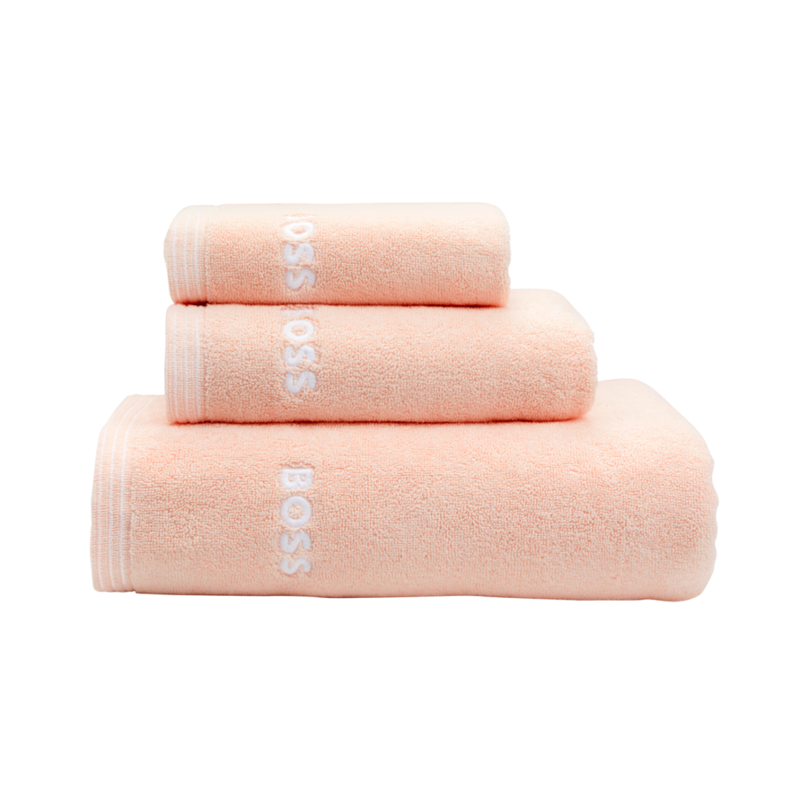 Trois serviettes couleur pêche empilées, chacune portant la marque « BOSS » brodée, sur un fond blanc uni.