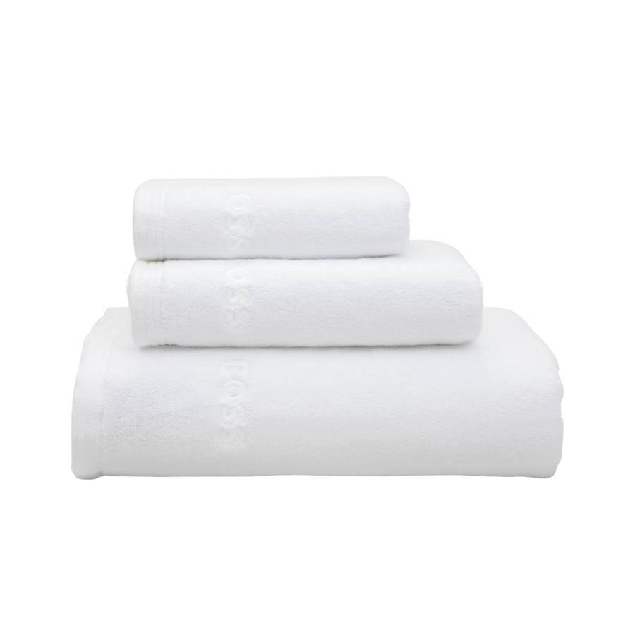 Une pile de trois serviettes de bain blanches unies, soigneusement pliées, de tailles différentes, sur fond blanc.