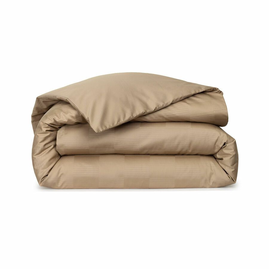 Une couette beige est empilée les unes sur les autres sur un fond blanc.